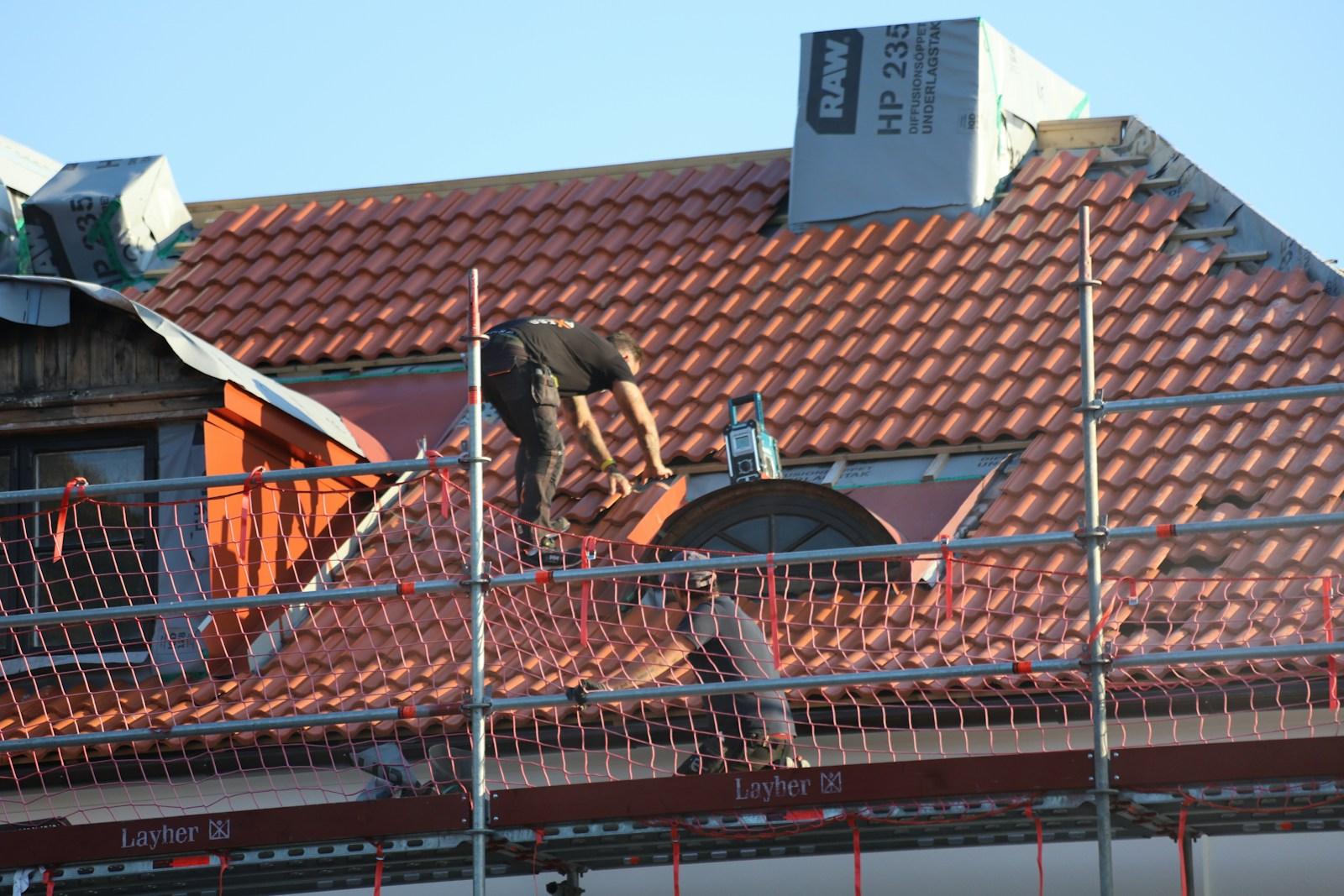 Dakwerker op een rood pannendak achter de veiligheidsleuning van een stelling
